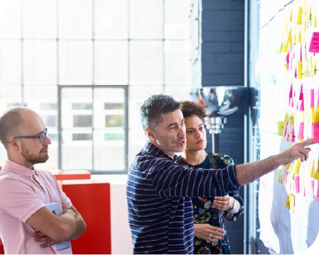 3 personnes travaillant devant un mur de post it 