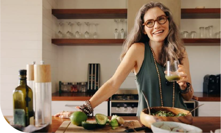 une femme souriante dans sa cuisine buvant un jus de fruit