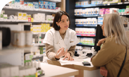 Une pharmacienne au comptoir discutant avec une cliente