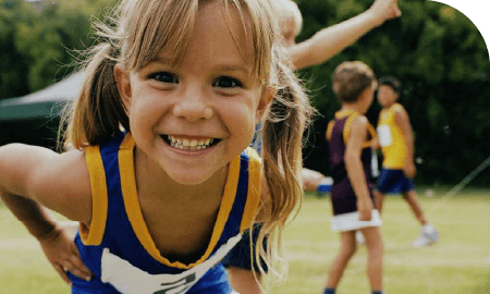 enfants jouant en extérieur et en maillots de sport. Au premier plan une petite fille qui sourit à la caméra