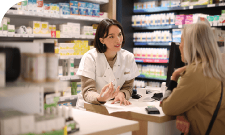 Une pharmacienne au comptoir discutant avec une cliente
