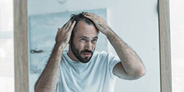 Homme qui constate la perte de ses cheveux devant un miroir