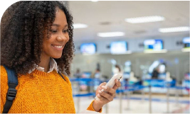 Une femme souriante dans un terminal d'aéroport qui utilise son téléphone 